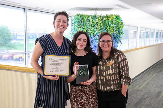 Three people stand with and award.